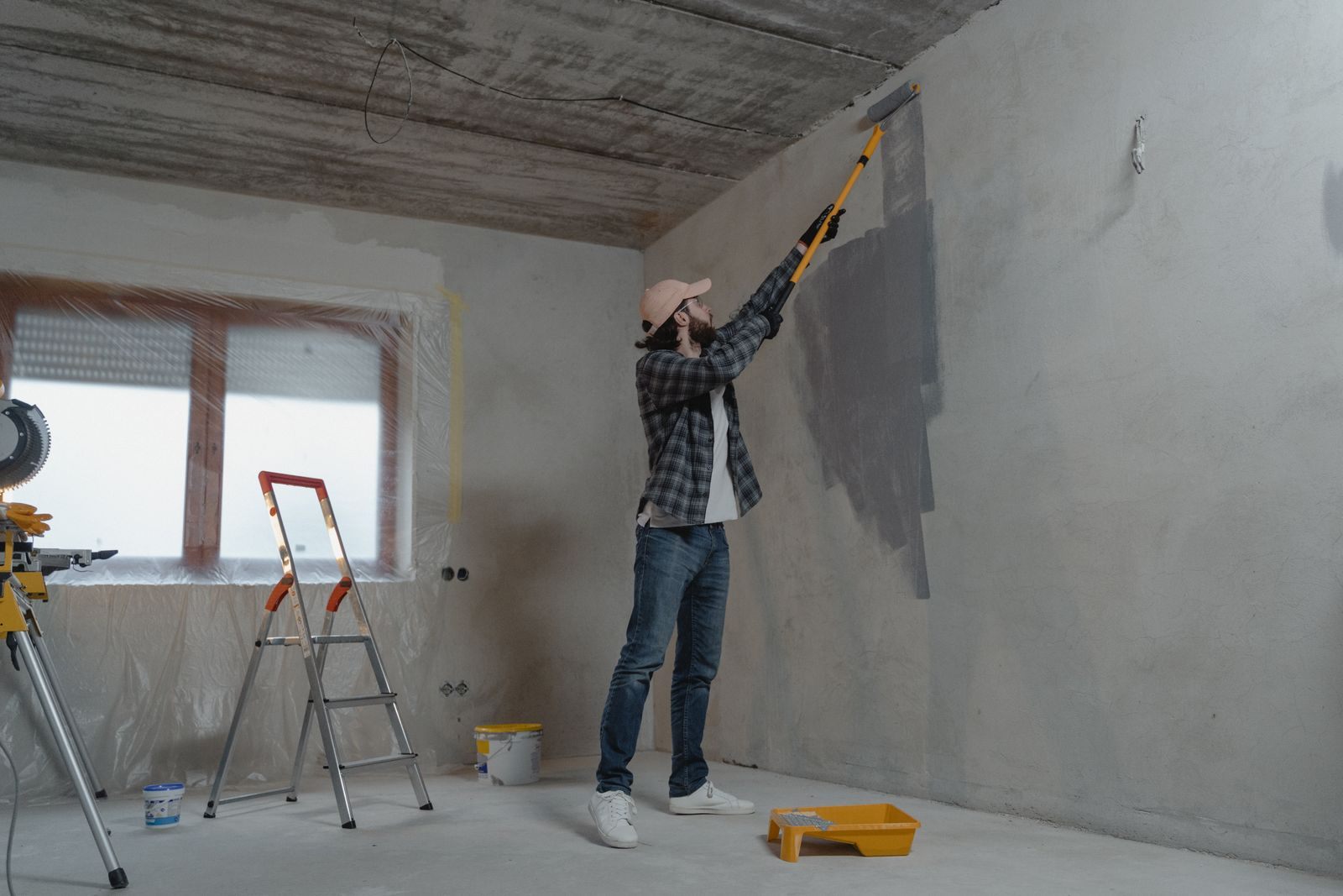 A man painting an interior wall with a roller during a home renovation project
