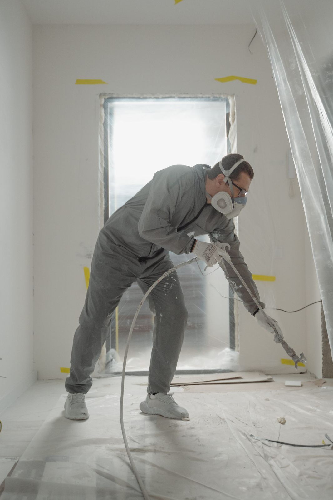 Worker applying paint with a spray gun in a protected indoor renovation site
